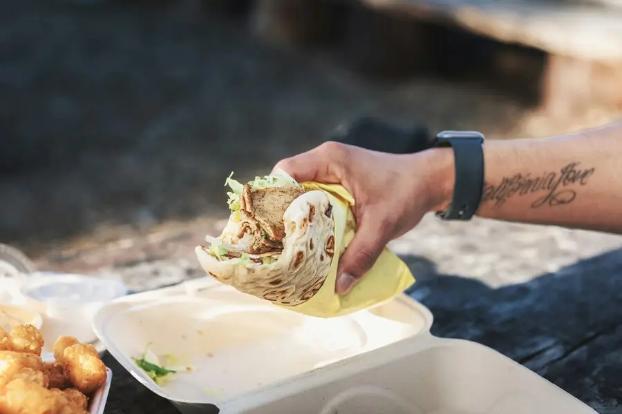 A hand holds a taco over a styrofoam container filled with food.