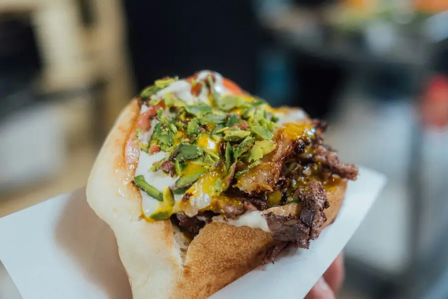A close-up of a pita sandwich filled with meat, vegetables, and sauce, topped with herbs and a dollop of yogurt.