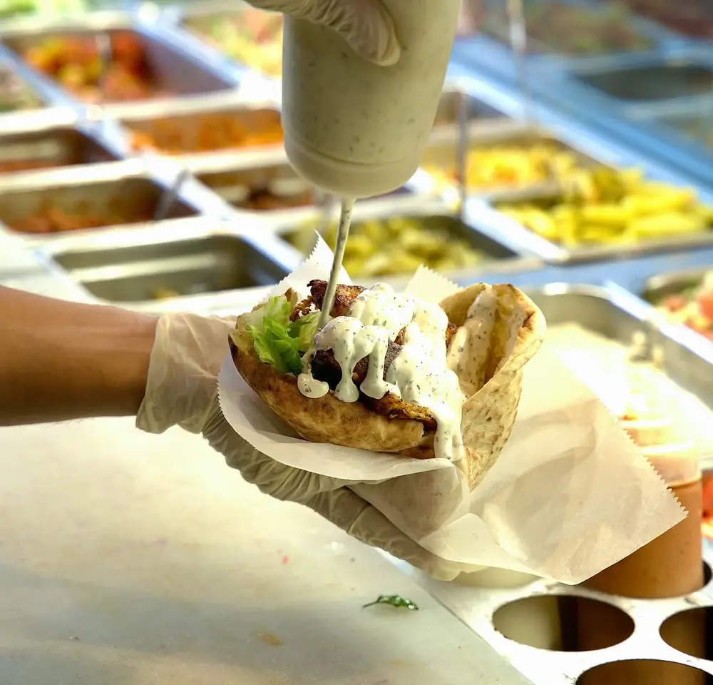 Chicken shawarma pita drizzled with garlic sauce being finished at the topping bar