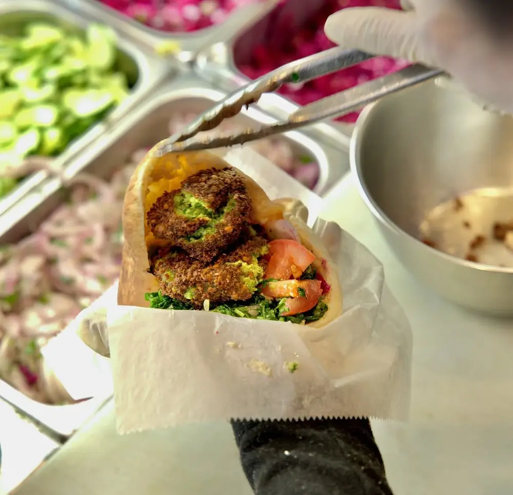 Falafel pita with fresh parsley, tomato and greens held at the topping bar