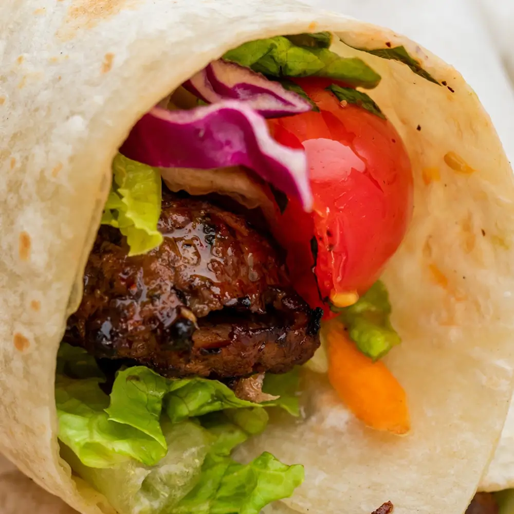 A close-up of a wrap filled with grilled meat, lettuce, tomato, and red onion.