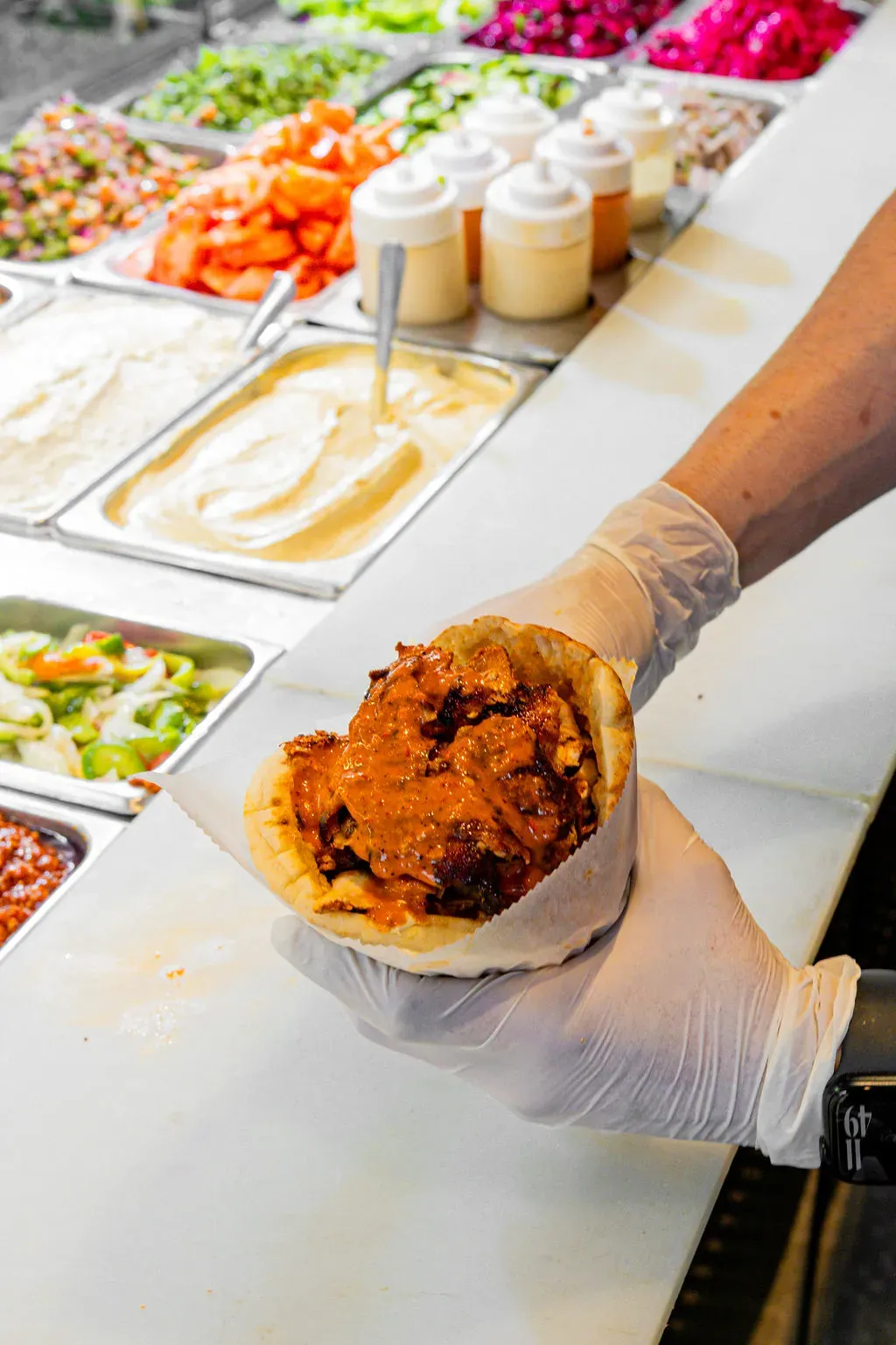 Chicken shawarma pita with spicy sauce held over the topping bar with sauces and fresh salads