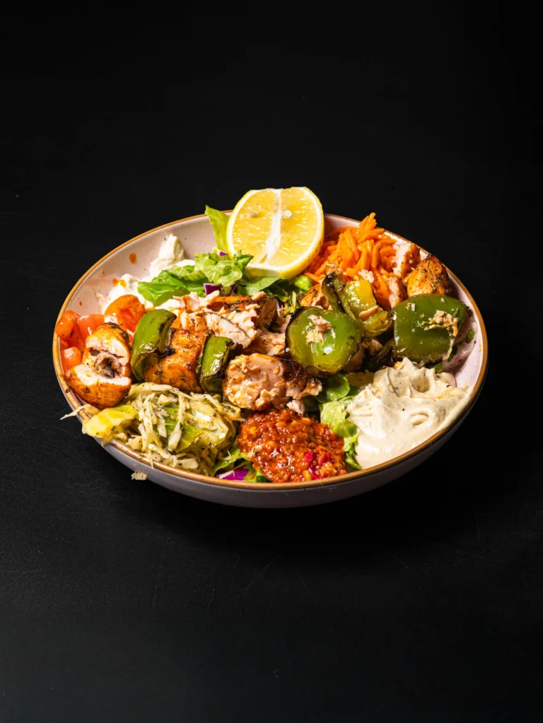 Grilled chicken kebab bowl with green peppers, hummus, salad and carrots on dark background