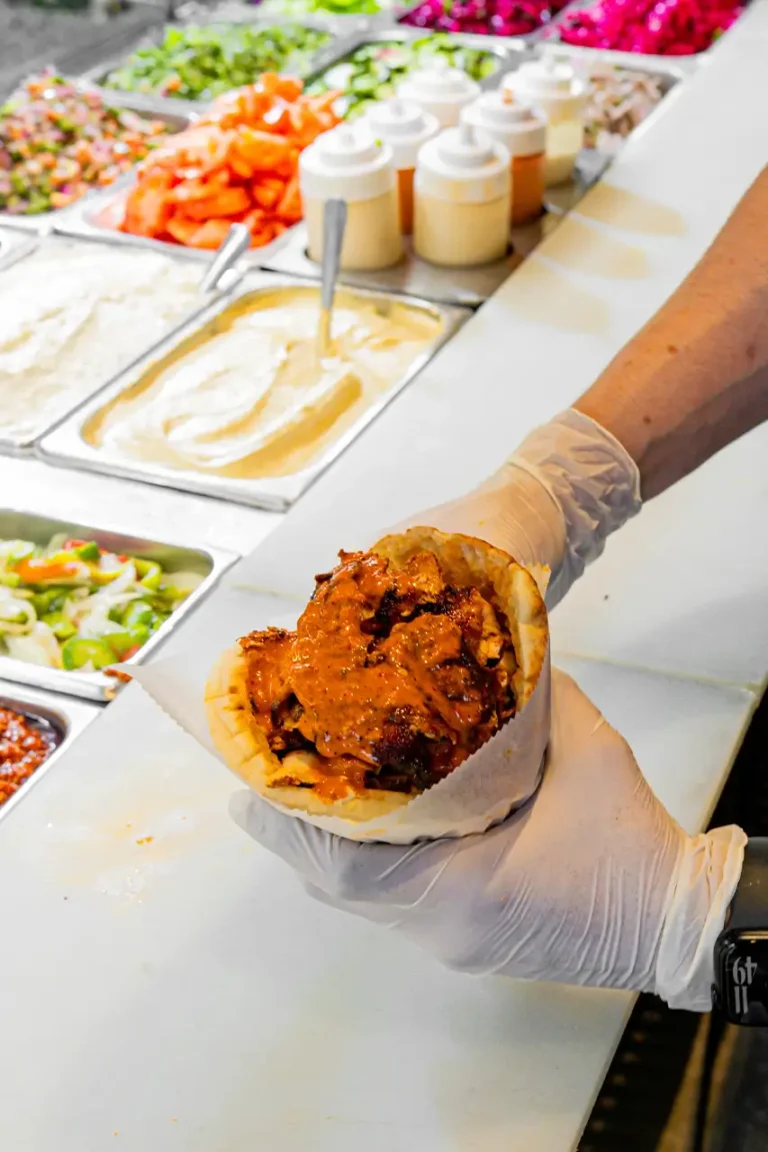 Chicken shawarma wrap with spicy sauce held over the topping bar with sauces and fresh vegetables