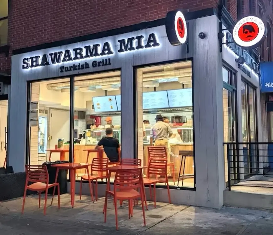 Shawarma Mia Turkish Grill lit up at night with customers ordering and red patio seating outside