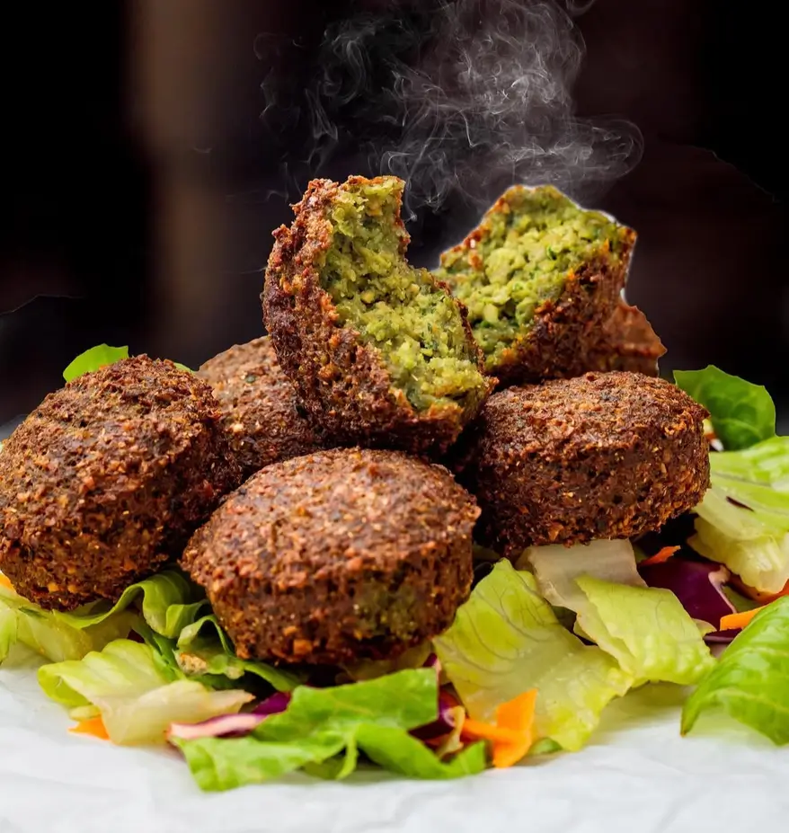 Fresh hot falafel on a bed of lettuce, red cabbage and carrot, one broken open to show the inside