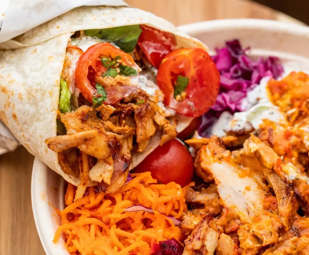 A wrap with shredded carrots, chicken, tomatoes, and red cabbage in a white bowl.