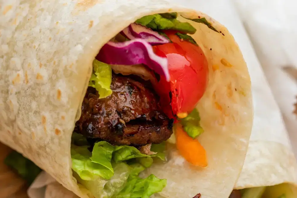 Lamb kofta kebab wrap with lettuce, tomato, red cabbage and carrot in flatbread