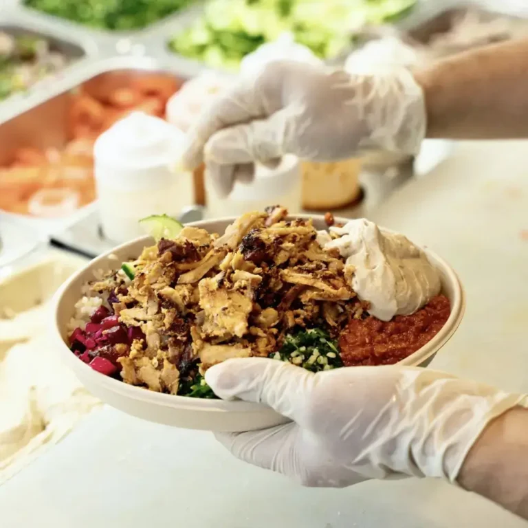 Chicken shawarma bowl with rice, hummus, tabbouleh, red cabbage and hot sauce being assembled