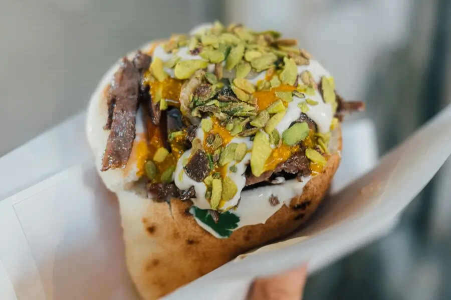A loaded baked potato with meat, cheese, sour cream, and chopped nuts.