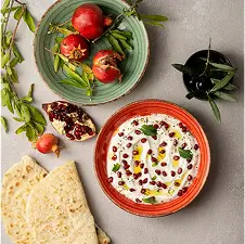 Creamy yogurt dip topped with pomegranate seeds and olive oil, served with pita and fresh pomegranate