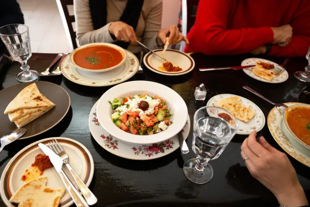 Table set with shepherd salad, tomato soup, flatbread, and dips as people share a meal