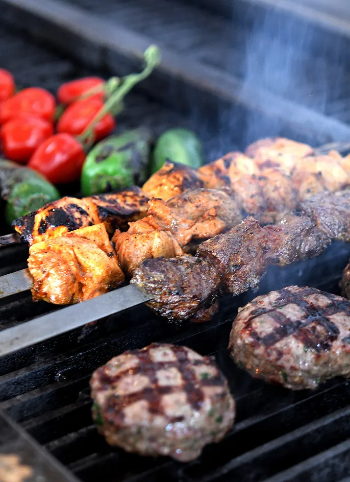 Chicken and lamb shish kebabs with koftas, peppers and tomatoes smoking on the grill