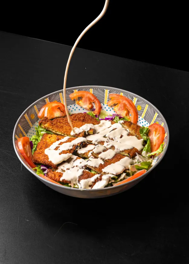 Tahini sauce drizzled over breaded cutlets on a salad bowl with tomato and lettuce