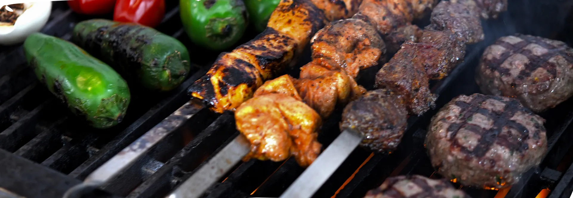 Chicken and lamb shish kebabs, koftas and green peppers grilling over open flames